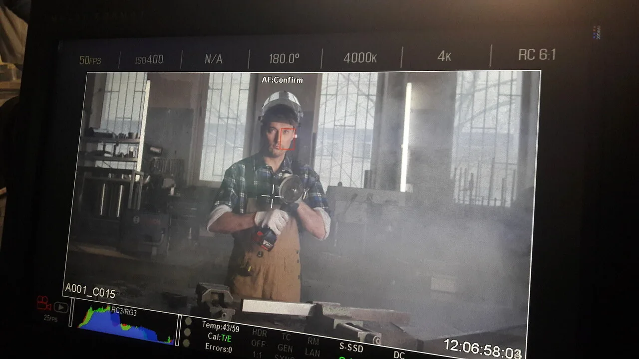 A monitor shows an actor in workwear holding a tool in a workshop.