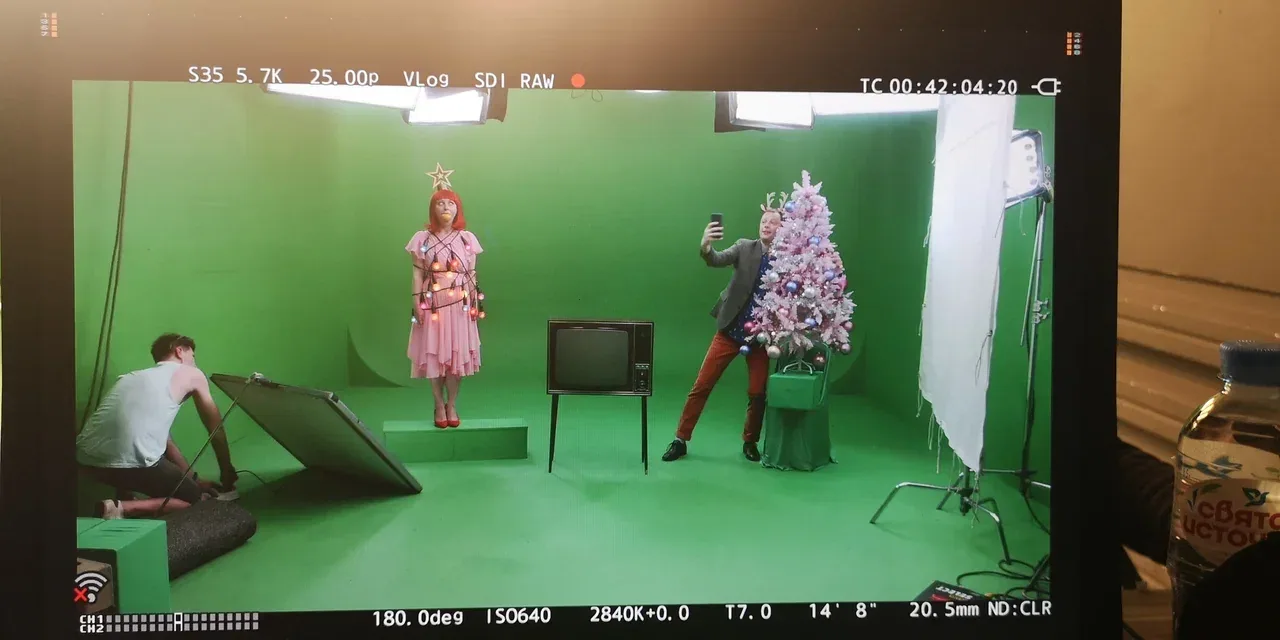 A monitor shows performers, a Christmas tree, a television and props on a green-screen stage.