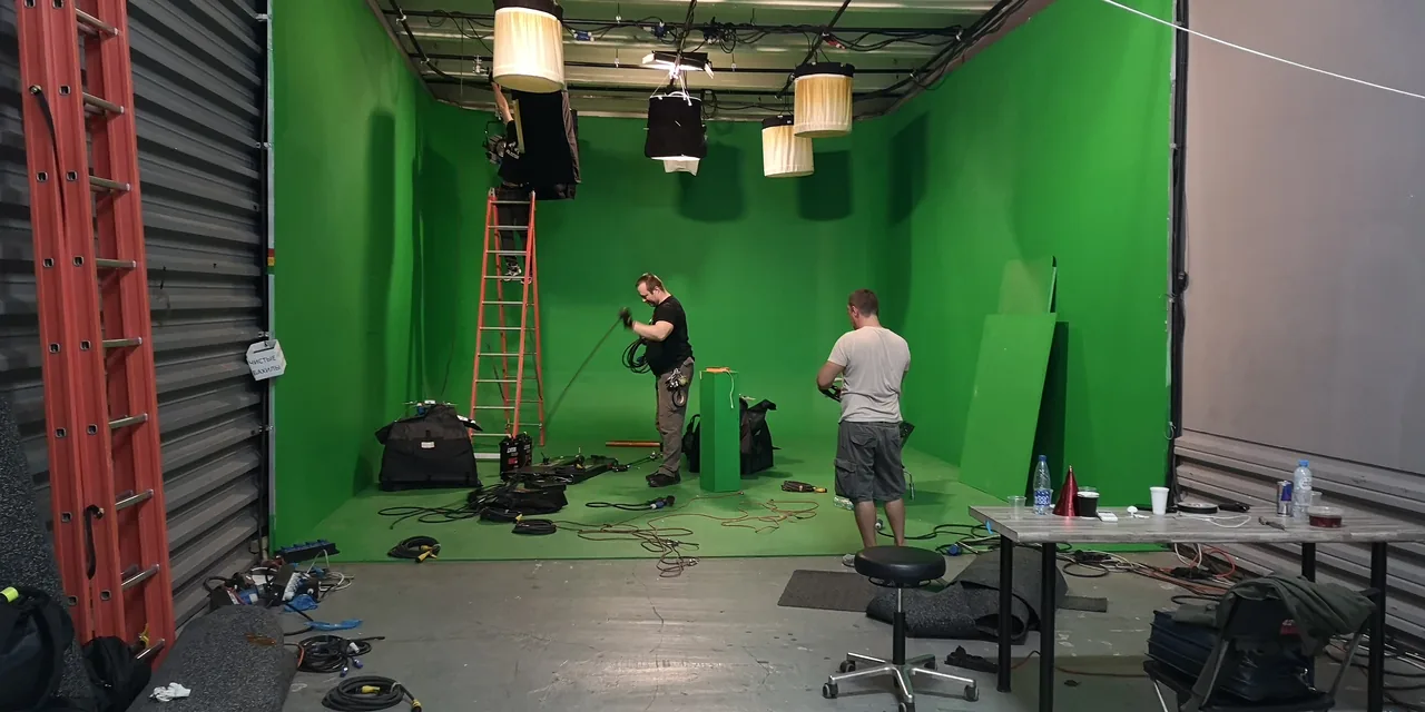A green-screen stage with lights, equipment and crew handling cables.