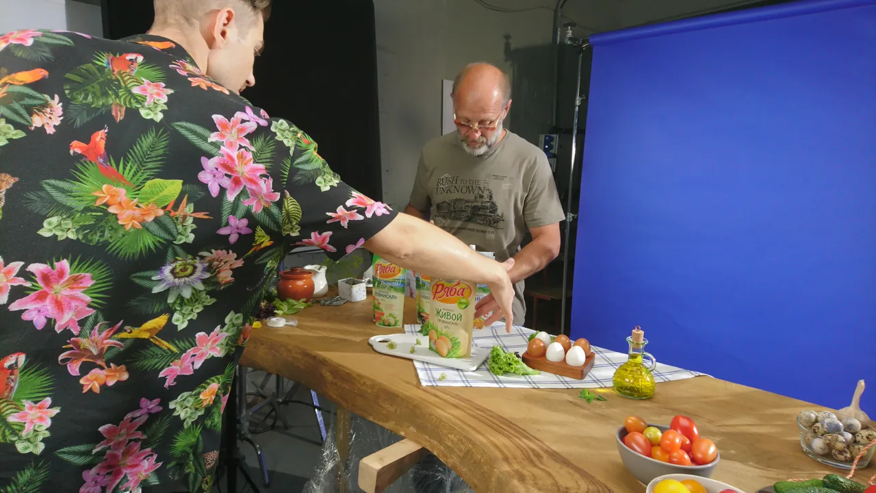 Two crew members arrange Ryaba packs and ingredients against a blue backdrop.