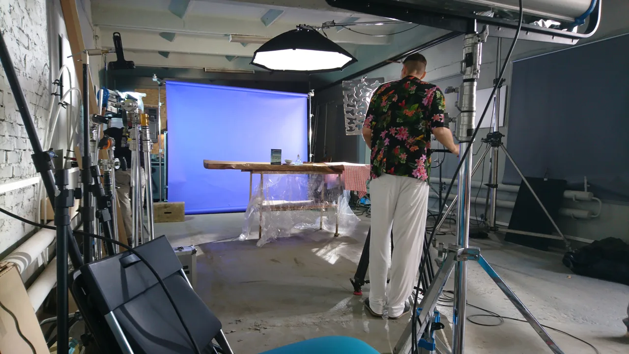 A studio with a product table, blue backdrop, lighting and a crew member.